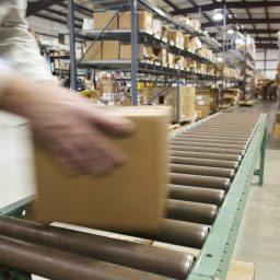 A person collects a box from the end of a conveyor belt in a warehouse setting